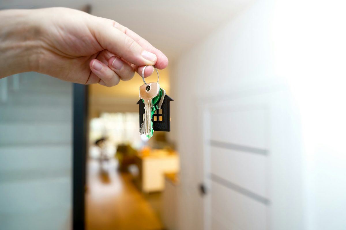 Buyer holding house keys in front of the entrance of a new home